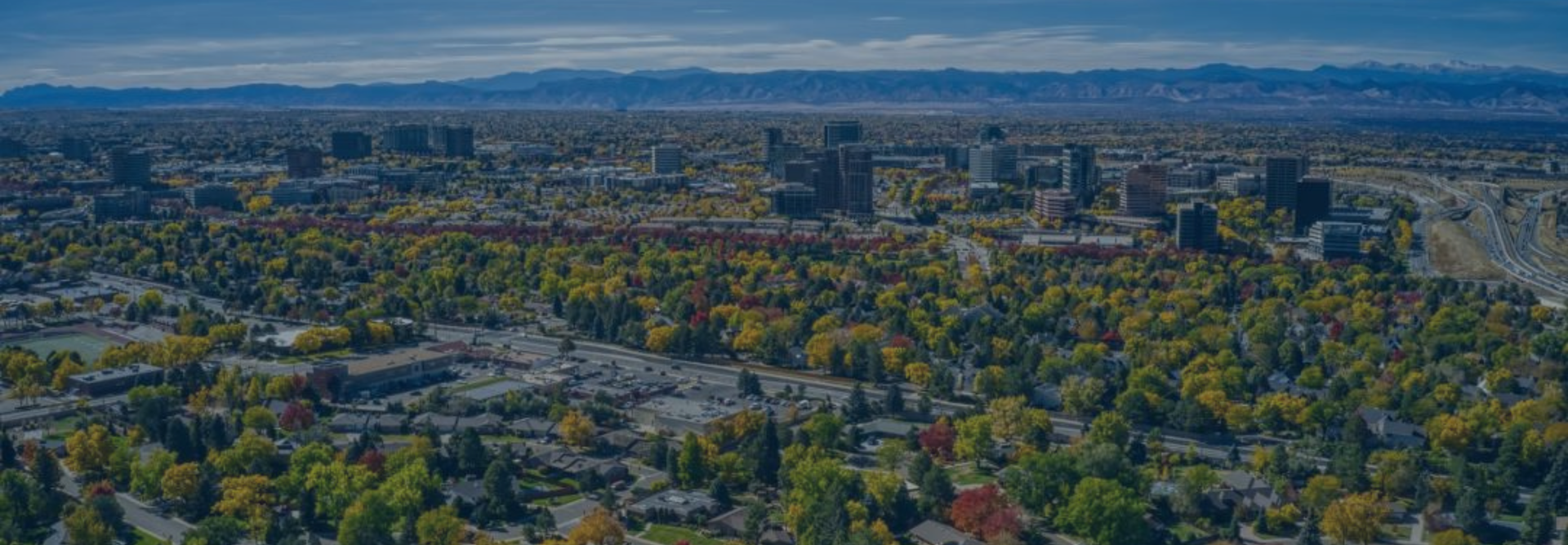 Wide shot of a city with many green trees, large buildings, and mountains in the background
